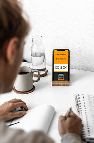 live-stream-begint-over-klein Mockup van een man aan een bureau. Op zijn telefoon staat te lezen: "live stream begint over 12:04 ComBron".